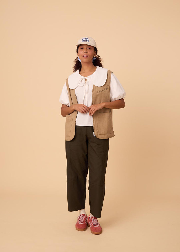 A straight size woman wearing a blouse with an exaggerated collar and green wide leg pants 