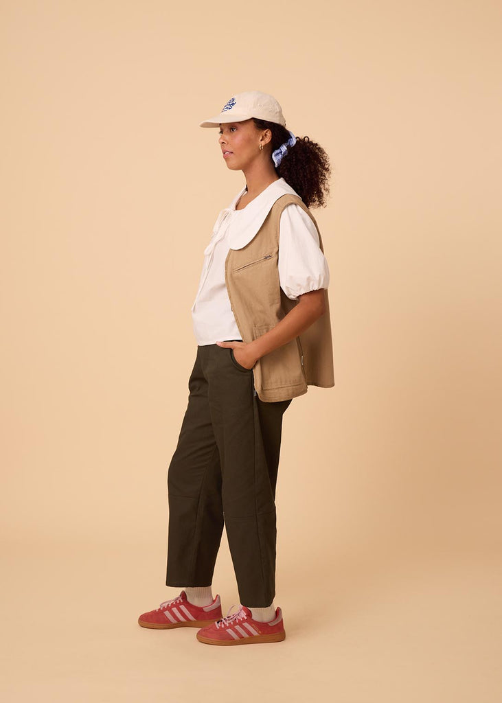 A straight size woman wearing a blouse with an exaggerated collar and green wide leg pants 