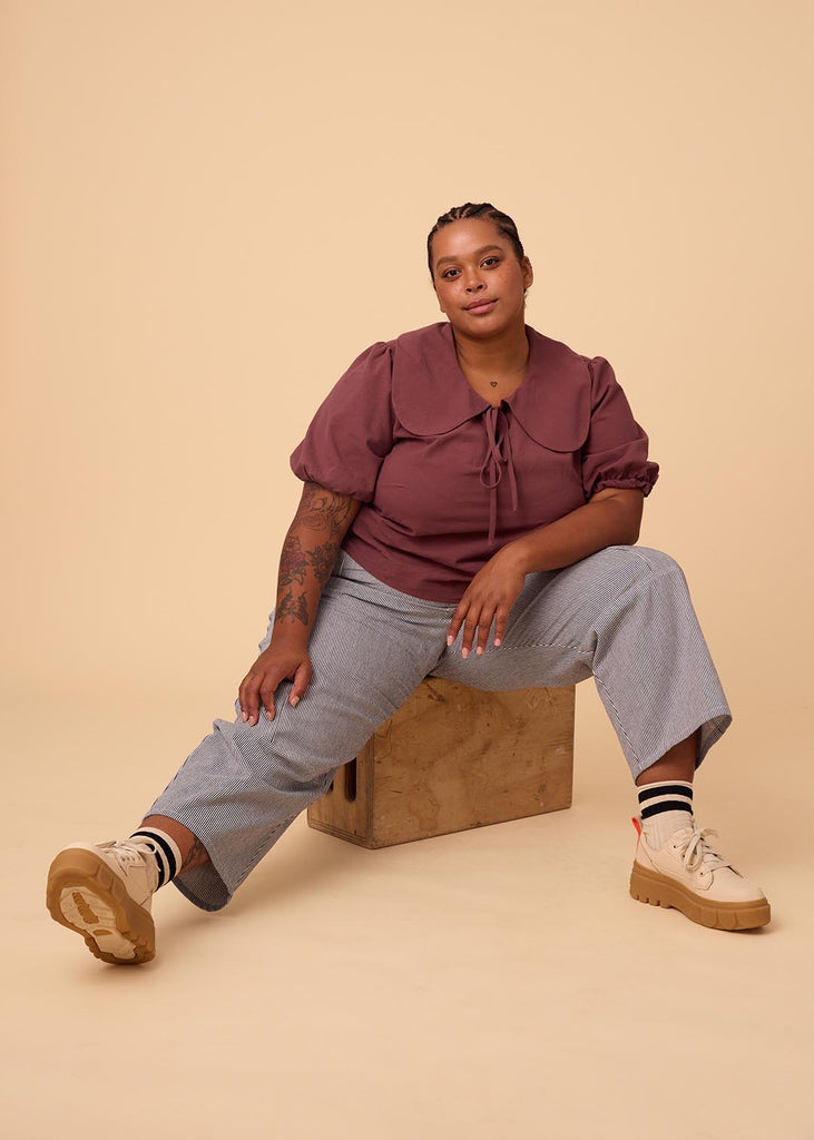 a plus size woman sitting down in a plum blouse with an exaggerated collar