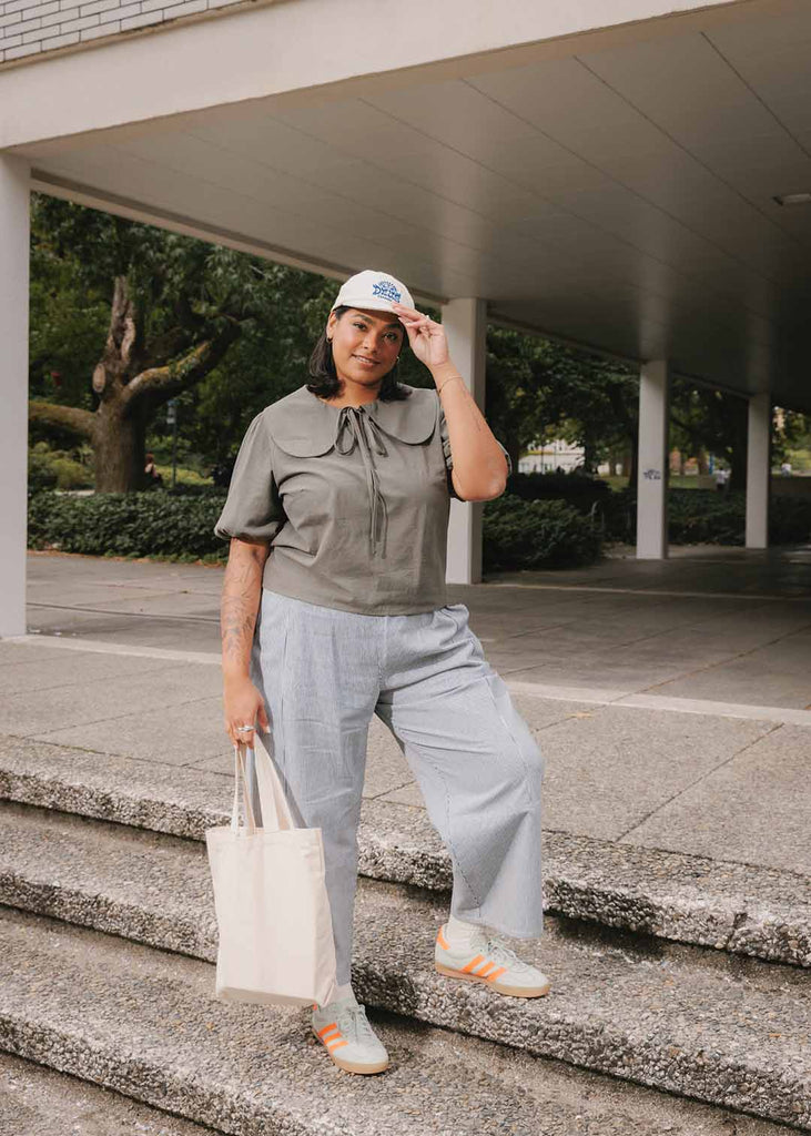 A mid size woman wearing a blouse with an exaggerated collar and striped wide leg pants 