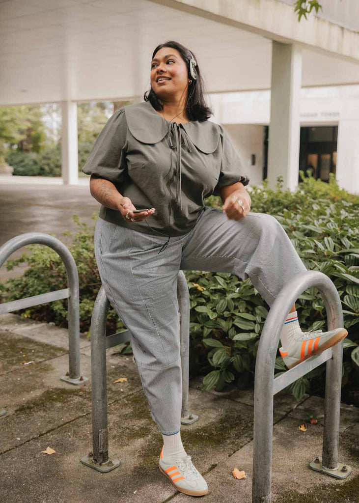 A plus size woman wearing a blouse with an exaggerated collar and railroad stripe wide leg pants 