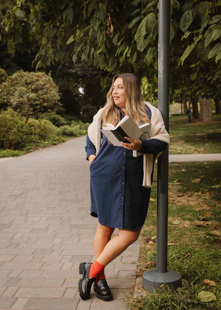 plus size person in a navy shirt dress holding books