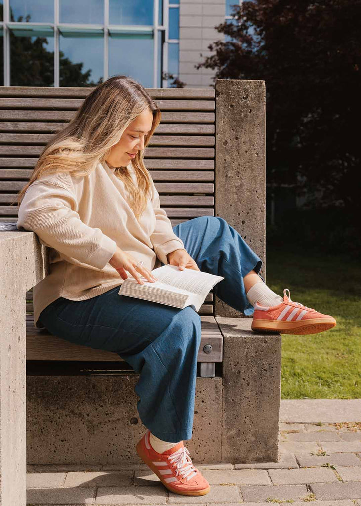 plus size woman sitting on a bench reading wearing cream long sleeve waffle shirt