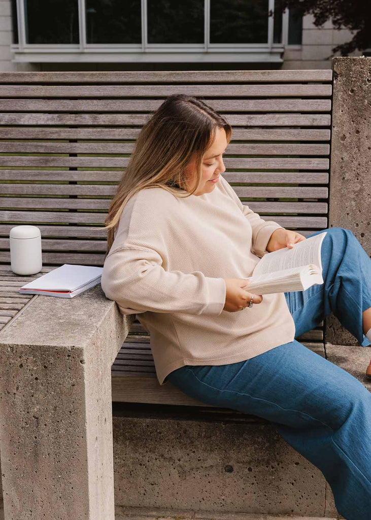 plus size woman sitting on a bench reading wearing cream long sleeve waffle shirt