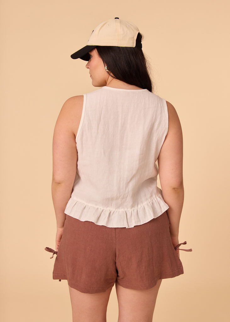 a straight sized woman wearing a white linen tank top and brown shorts