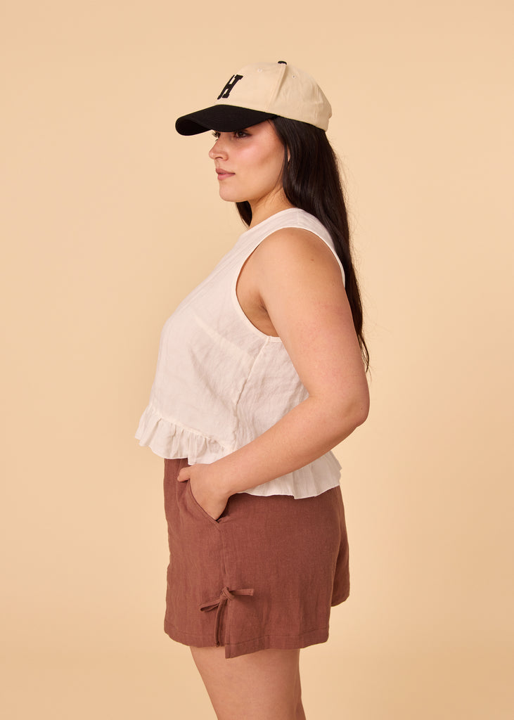 a straight sized woman wearing a white linen tank top and brown shorts