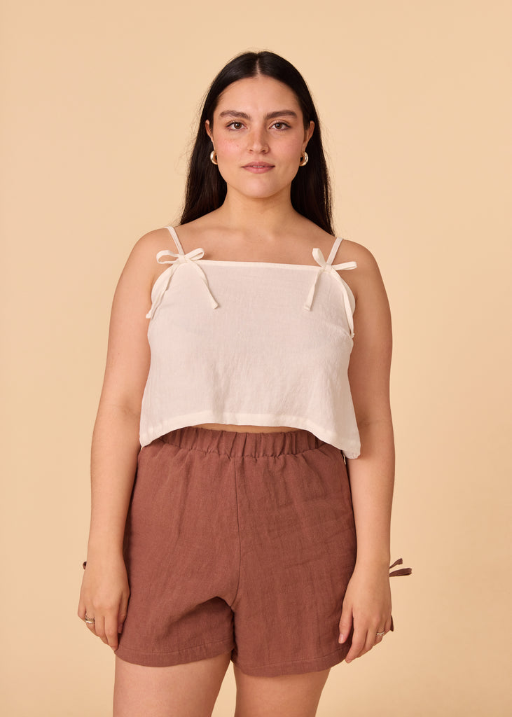 a straight size woman wearing a white cropped tank top and brown shorts